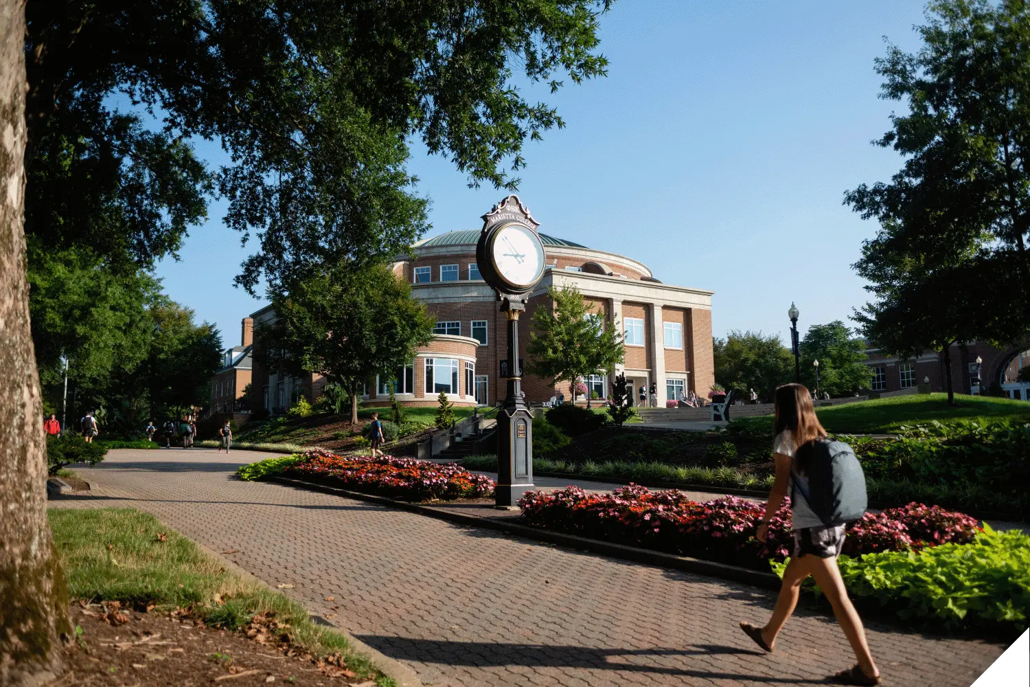 A student walking on the Christy Mall with a clock and the Legacy Library in the background