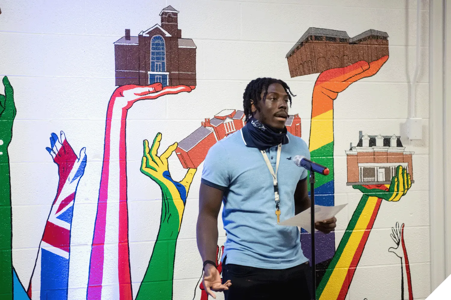 A student speaking into a microphone while standing in front of the diversity mural inside the Multicultural Center.