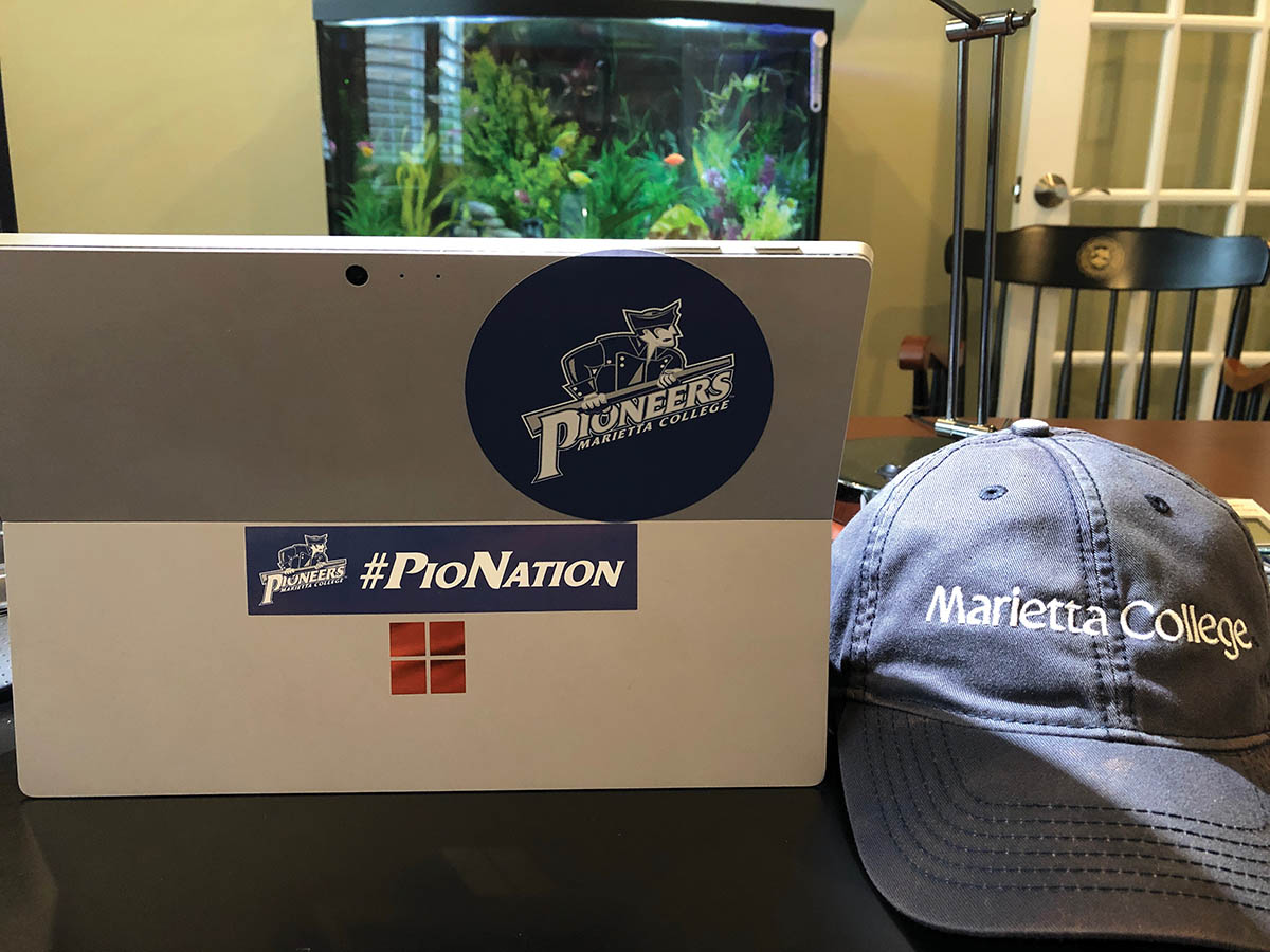 Marietta College Pioneer hat next to pio stickers on the back of a computer