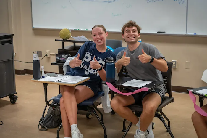 Two Marietta College students smiling and giving thumbs up in a classroom