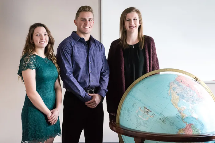 3 Marietta students standing behind a large globe