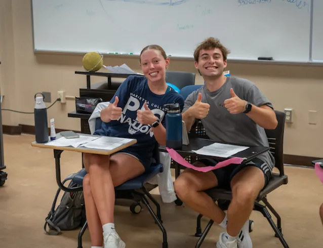 Two Marietta College students smiling and giving thumbs up in a classroom