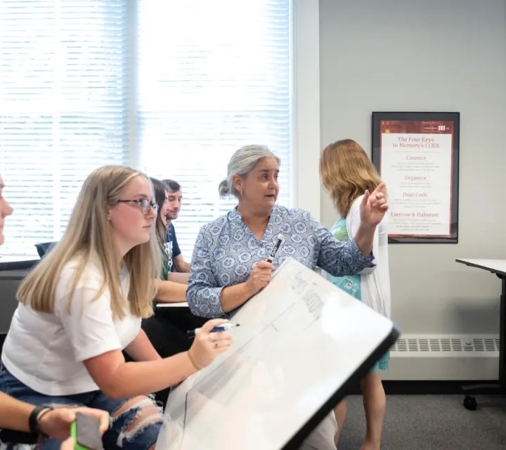 A Marietta College Education professor stands near students and points to the whiteboard