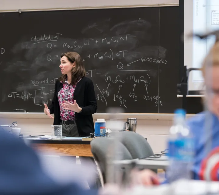 Professor teaches a science class in front of a black board
