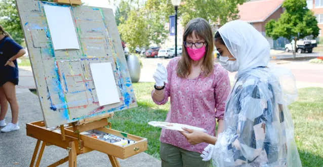 Faculty member Jolene Powell working with a student outside on an oil painting