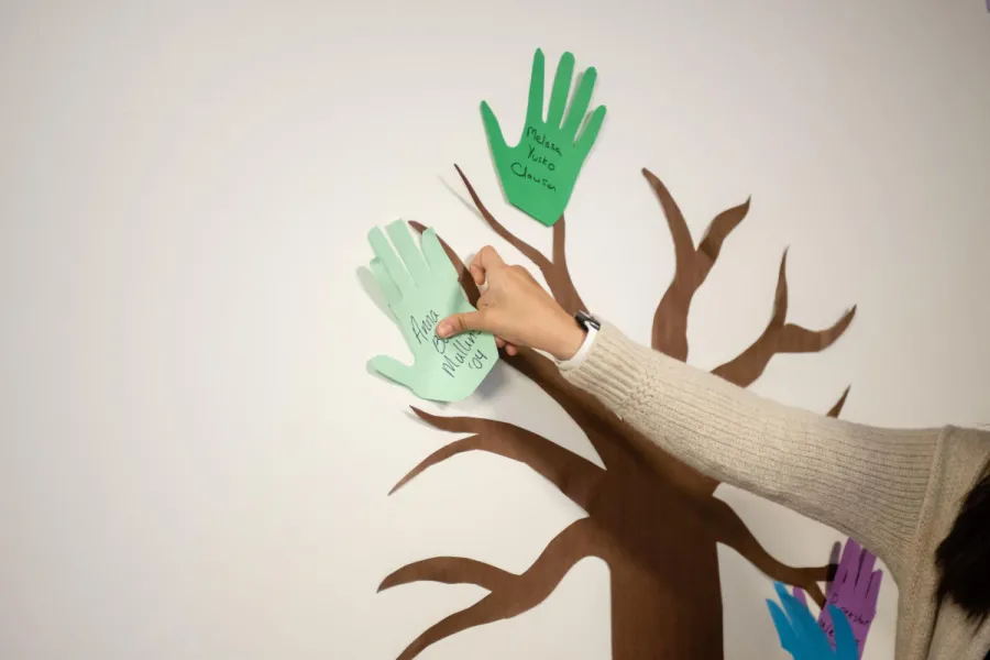 A hand places a paper hand on the wall to make the leaves of a giving tree mural