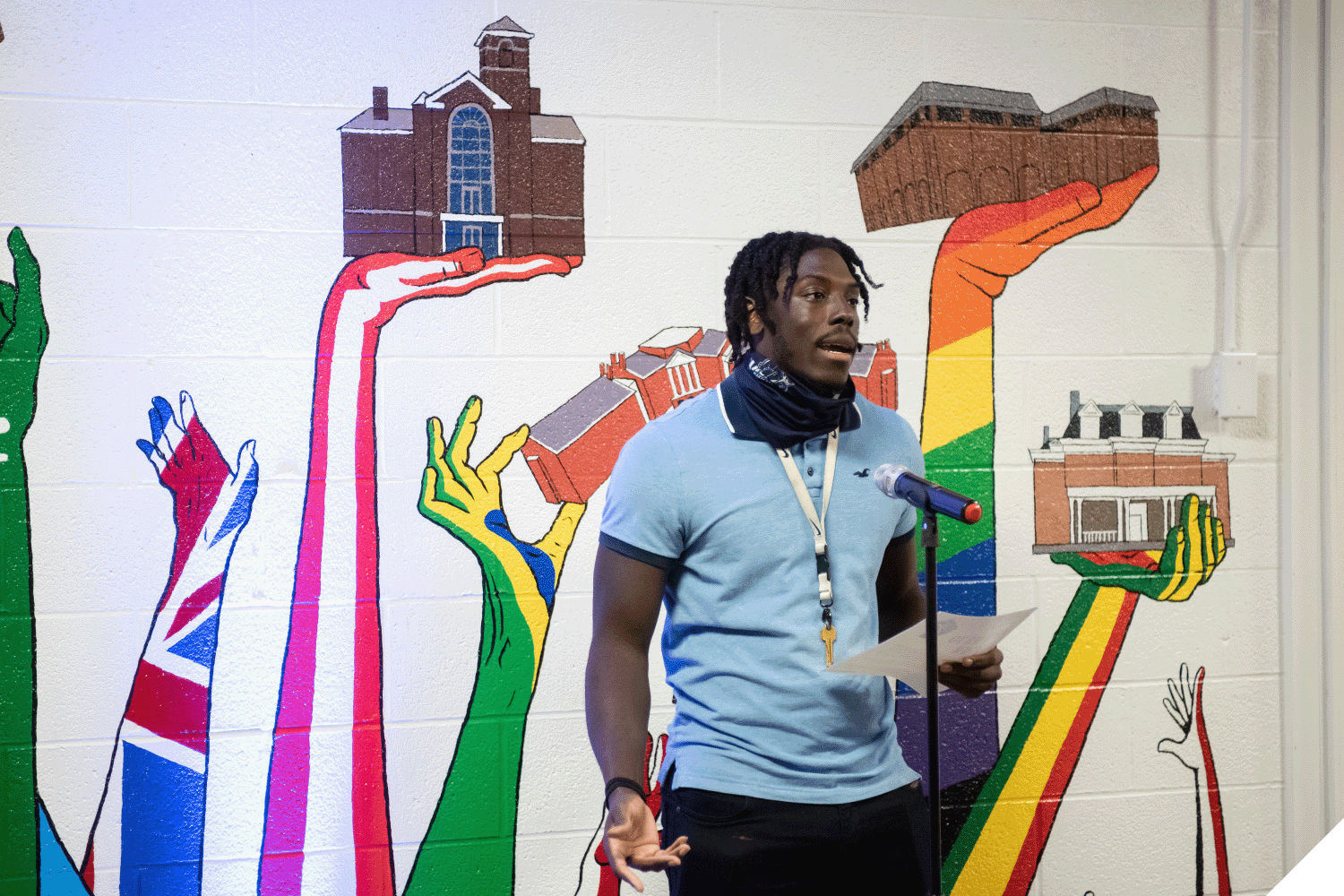 A student speaking into a microphone while standing in front of the diversity mural inside the Multicultural Center.