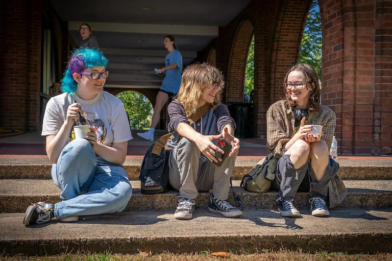Three Marietta College students sitting on the steps outside of Hermann Fine Arts Center