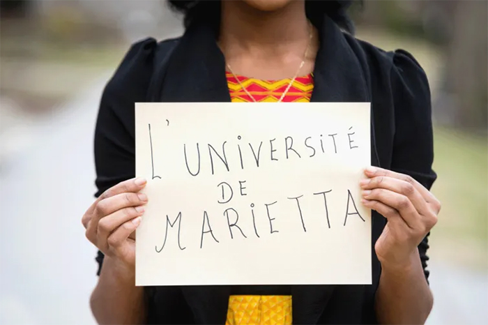 International student holds up sign proclaiming L' Universite de Marietta