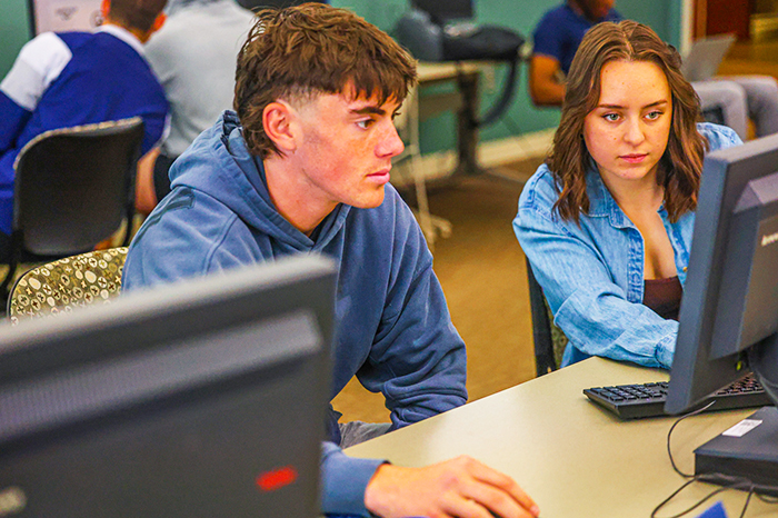 Two student work together at a computer monitor on an in-class assignment