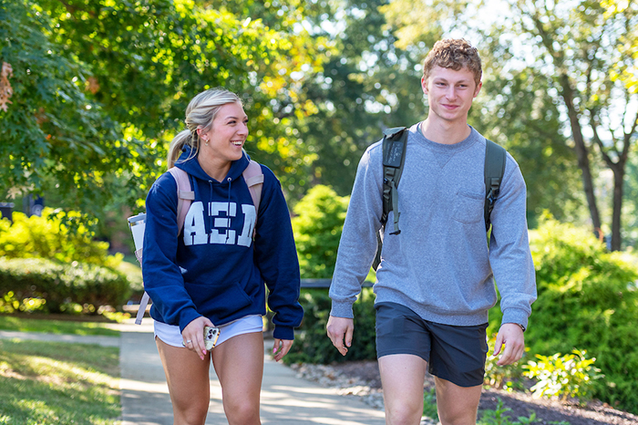 Two students walking across a tree-lined campus with backpacks
