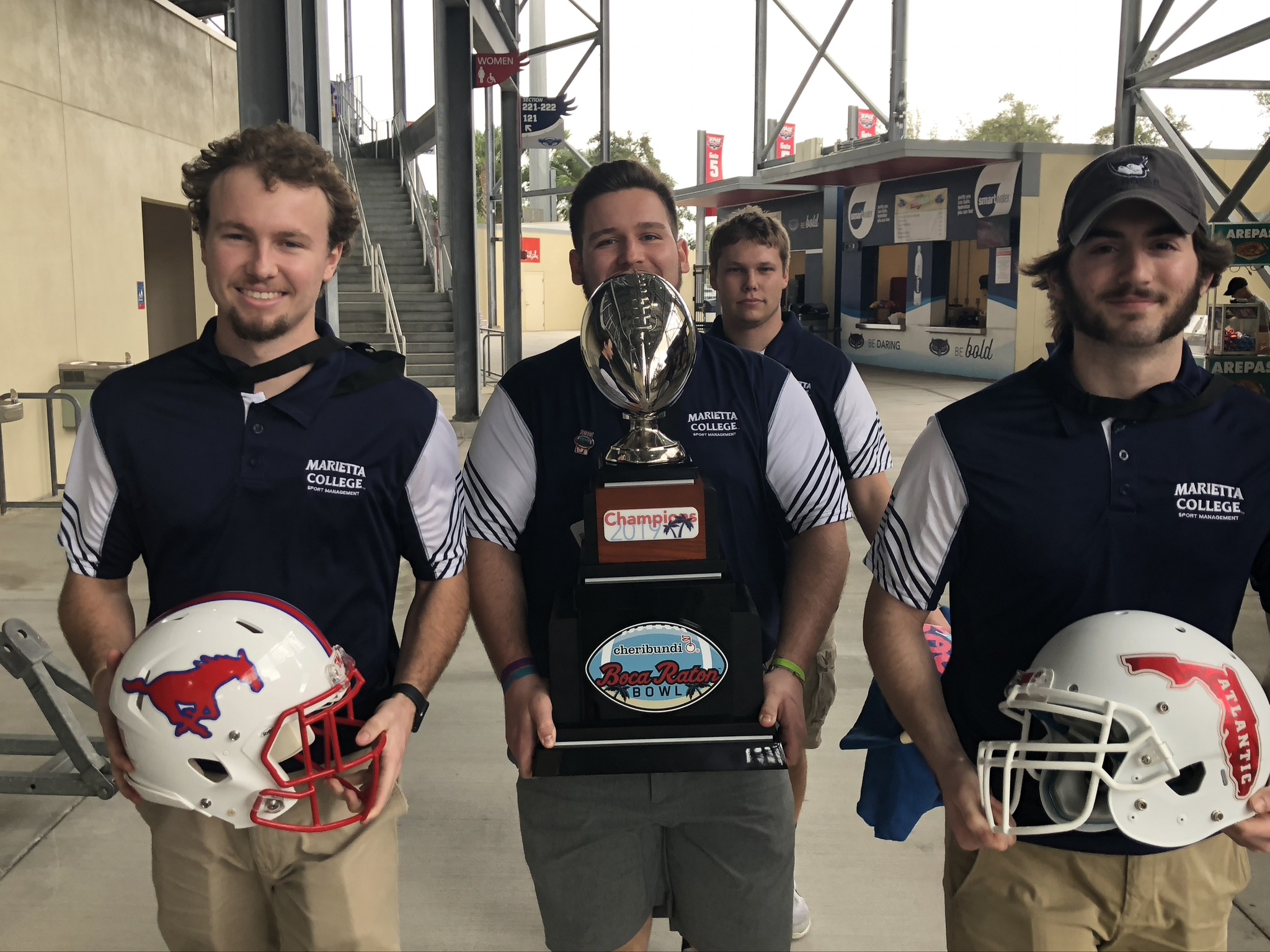 Marietta College Students job shadowing at the Boca Bowl pose with the game's trophy.