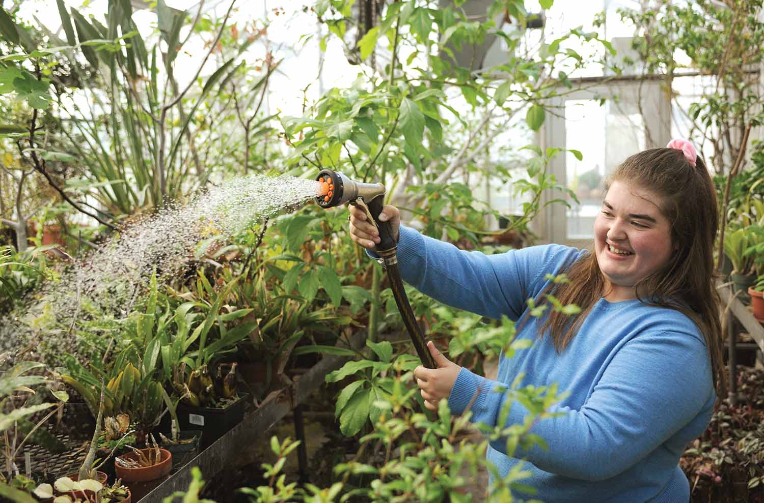 Morgan Tiller '23 waters plants with a hose in a greenhouse