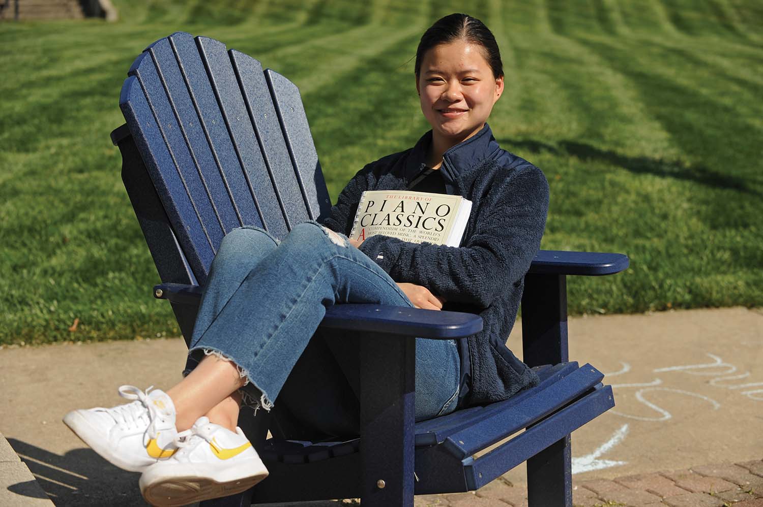 Marietta College student Sarah McNeer sits in a blue chair holding a booked titled Piano Classics