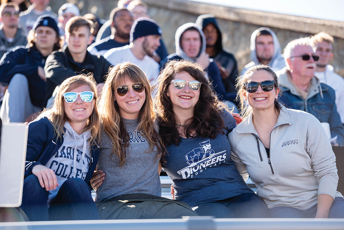  Caitlin Thomas, assistant coach for Track & Field; Raquel Ravaglioli, Director of Music Therapy; Katie Evans, Coordinator of Community Based Learning; and Katy Ely, Assistant Rowing Coach, take in a Saturday afternoon football game