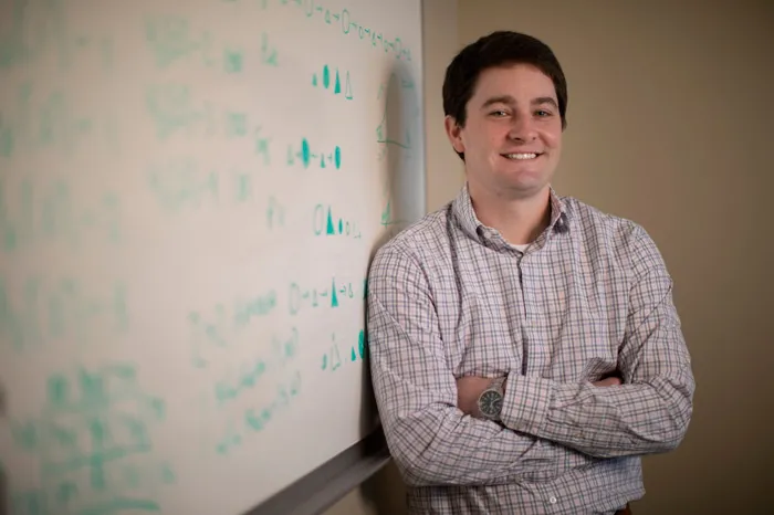 Faculty member Charles Doan leaning against a whiteboard