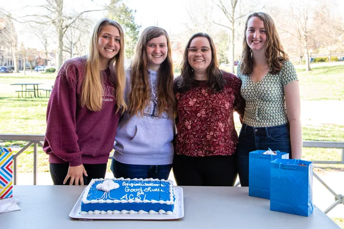 Four women students standing behind a cake