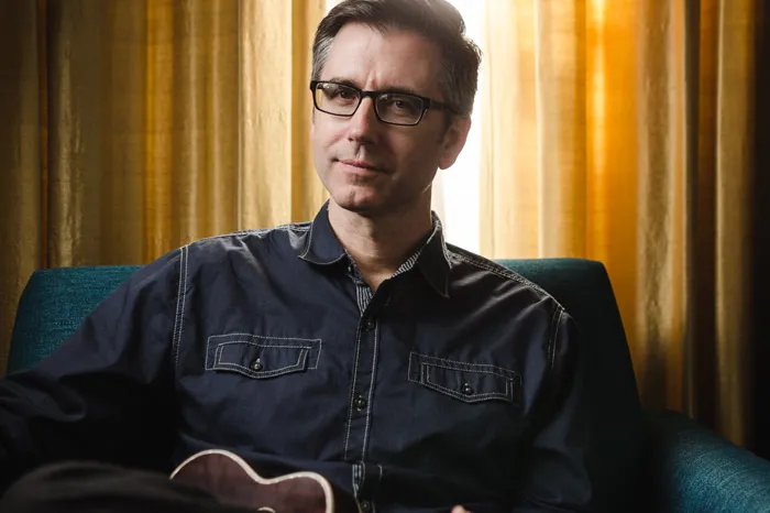 Todd Burge smiling, holding a guitar