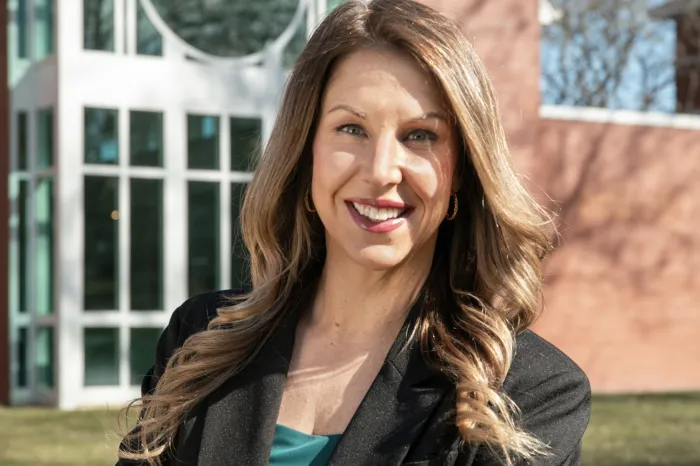 Lauren Thompson stands in front of a building, smiling, arms crossed in front of her.