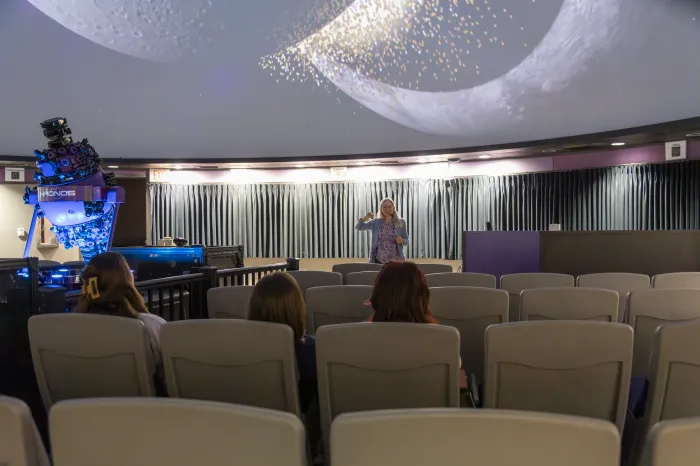 Professor Ann Bragg presents in the newly renovated planetarium. Three students sit in the audience. 