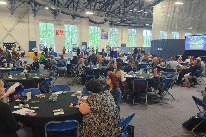 Attendees sit at round tables in the Dyson Baudo Recreation Center during the 2024 NonProfits LEAD Conference as a speaker stands on stage at the podium