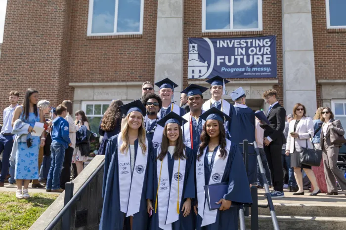 Marietta College graduates stand together happily in front of Legacy Library.