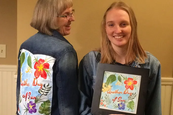Two women - one facing and the other with her back - showing off artwork on jean jacket