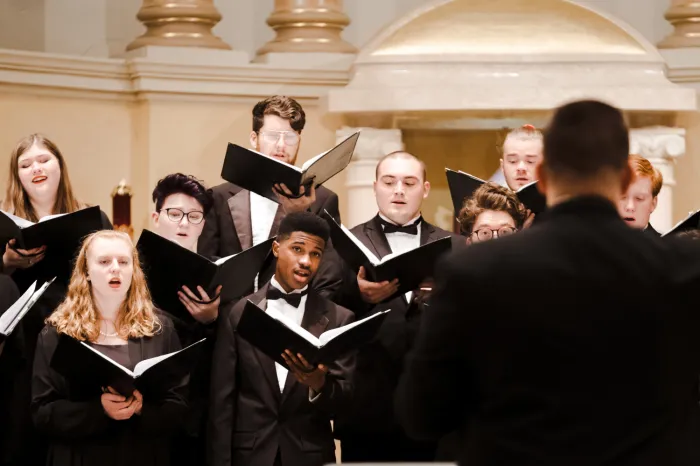 Multiple students singing while holding folders