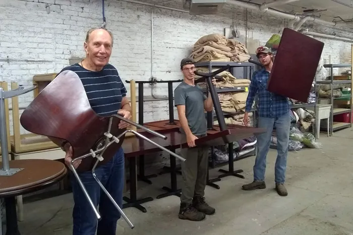 Three men carrying chairs and tables