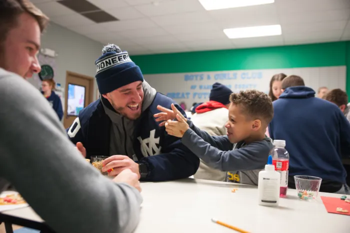 A Marietta College baseball player laughs with a child at the Boys & Girls Club
