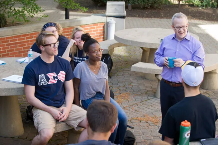 male professor with students outside on campus