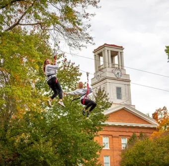 Marietta College students ride on a zipline in front of Erwin Hall
