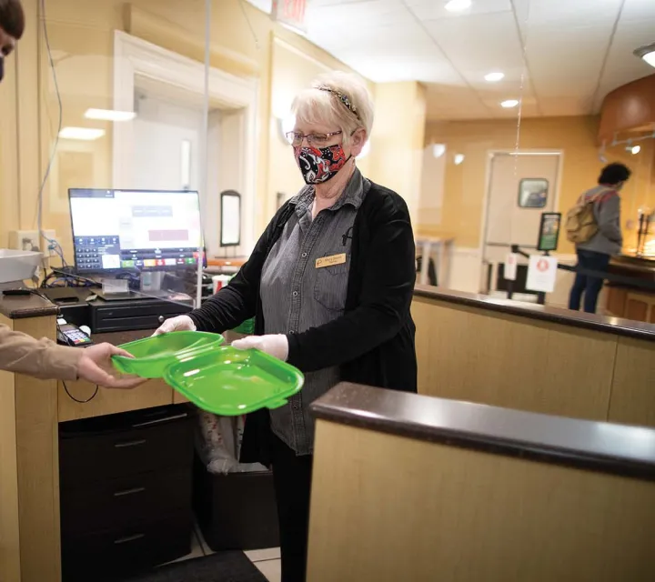 Cafeteria Worker hands a green to-go container to a student