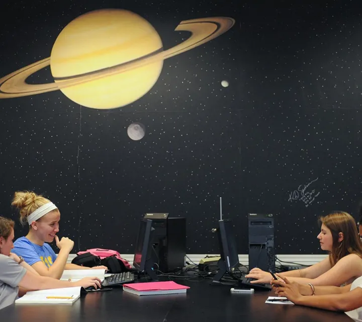 Marietta students in a science classroom with a mural of space behind them