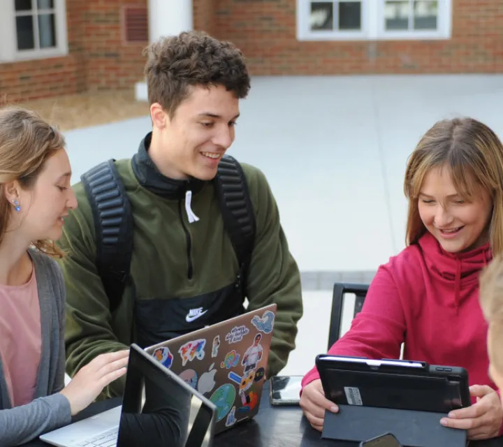 Students with laptops, tablets at a table studying