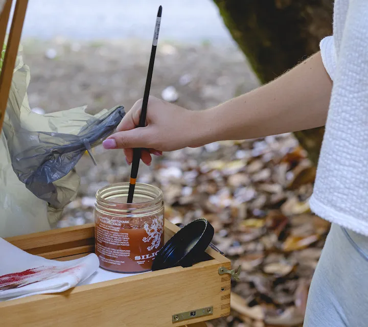 An art student dipping a paint brush in paint.