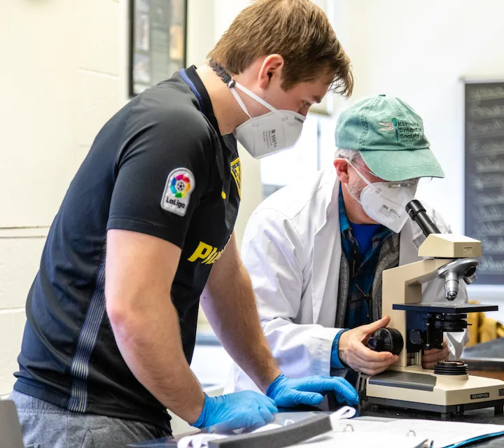 Professor Dave McShaffrey and a biology major looking at a slide in a microscope