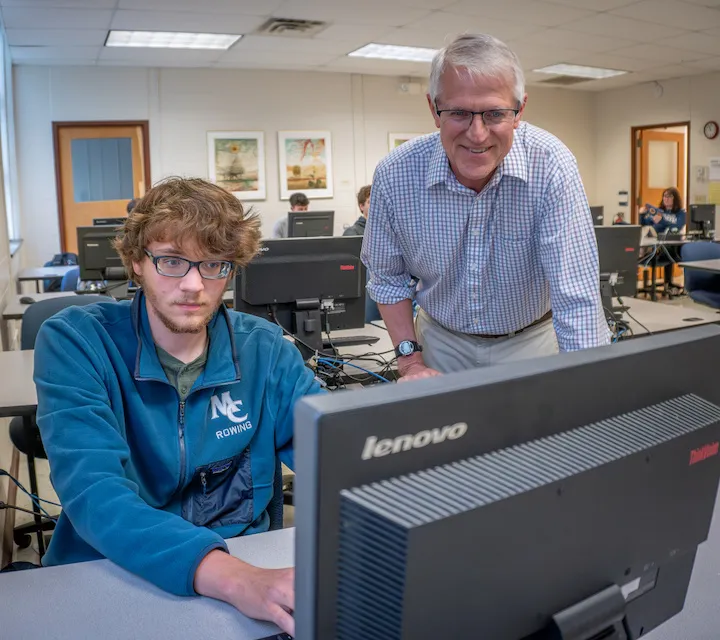 A Computer Science major works at a computer with Professor Bob Van Camp