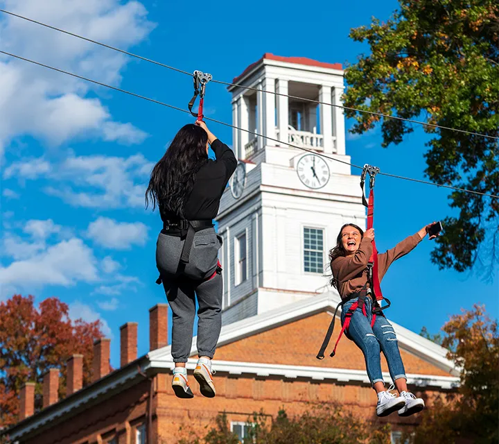 Two Marietta College Students zipline in front of Erwin Hall