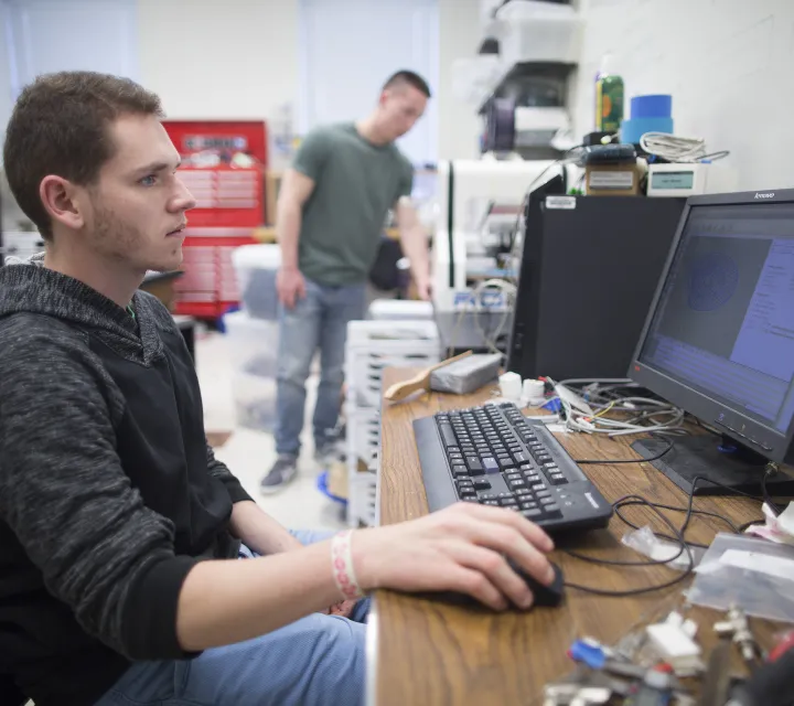 Student working at computer connected to 3D printer