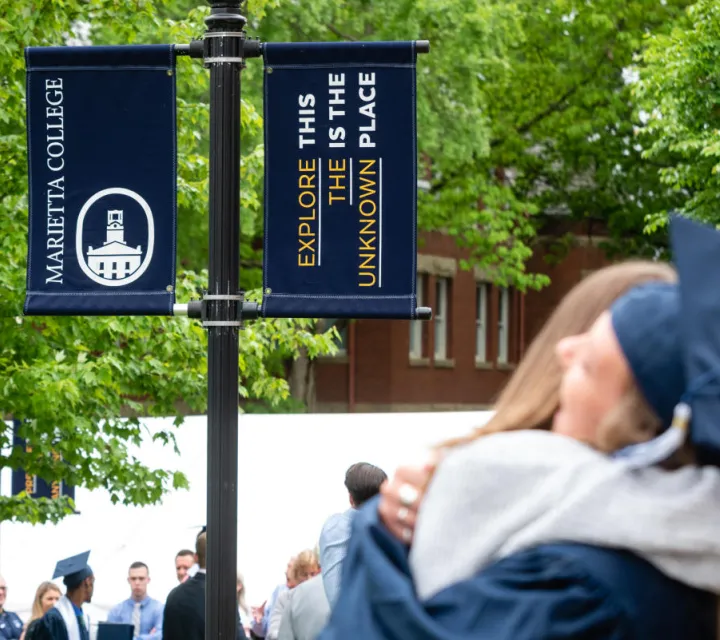 Marietta College banner above hugging graduates on commencement day