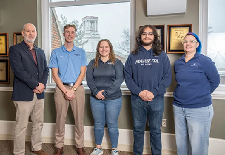 Three student and two advisors who researched healthcare consolidation pose in the library