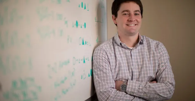 Faculty member Charles Doan leaning against a whiteboard