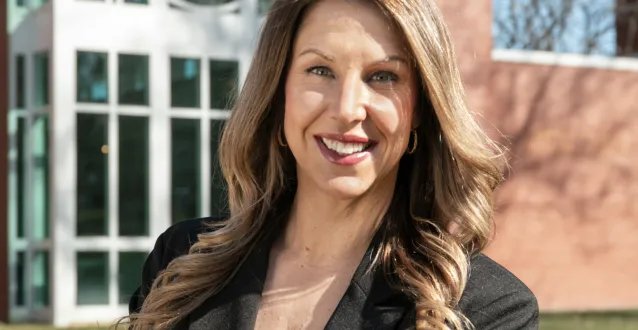 Lauren Thompson stands in front of a building, smiling, arms crossed in front of her.