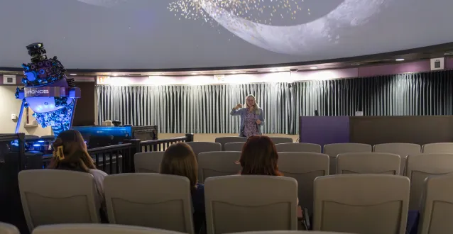 Professor Ann Bragg presents in the newly renovated planetarium. Three students sit in the audience. 