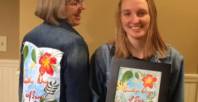 Two women - one facing and the other with her back - showing off artwork on jean jacket