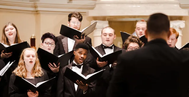 Multiple students singing while holding folders