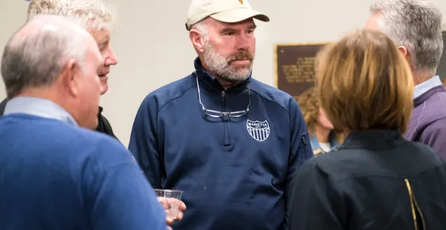 Alumnus Jeff Hugel speaks with other alumni at the boathouse