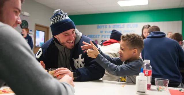 A Marietta College baseball player laughs with a child at the Boys & Girls Club