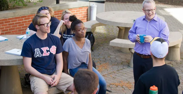 male professor with students outside on campus